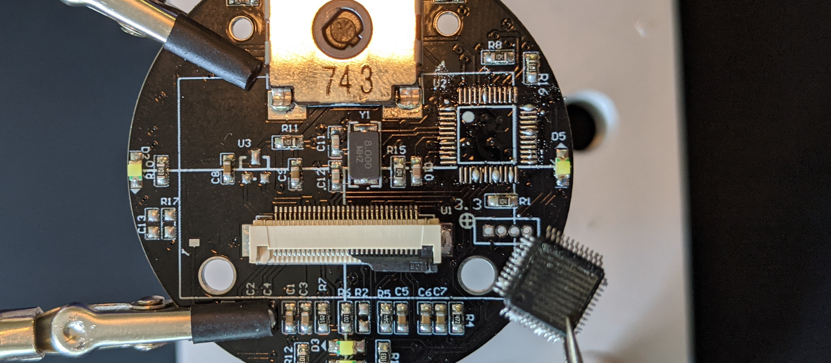 Photo of the original STM32 chip held in tweezers above the board, having been removed
